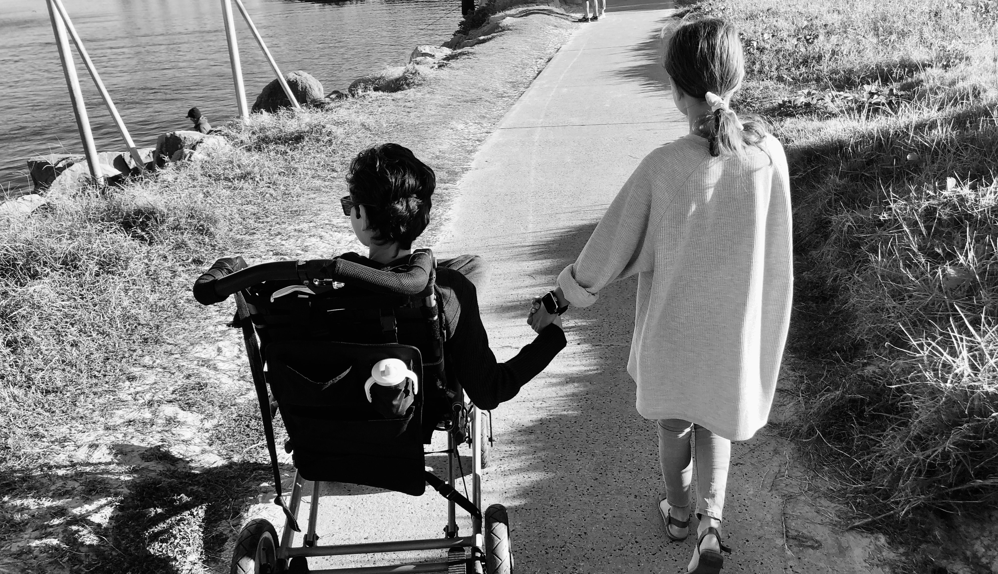 Two children walking together along a coastal path, one in an adaptive stroller